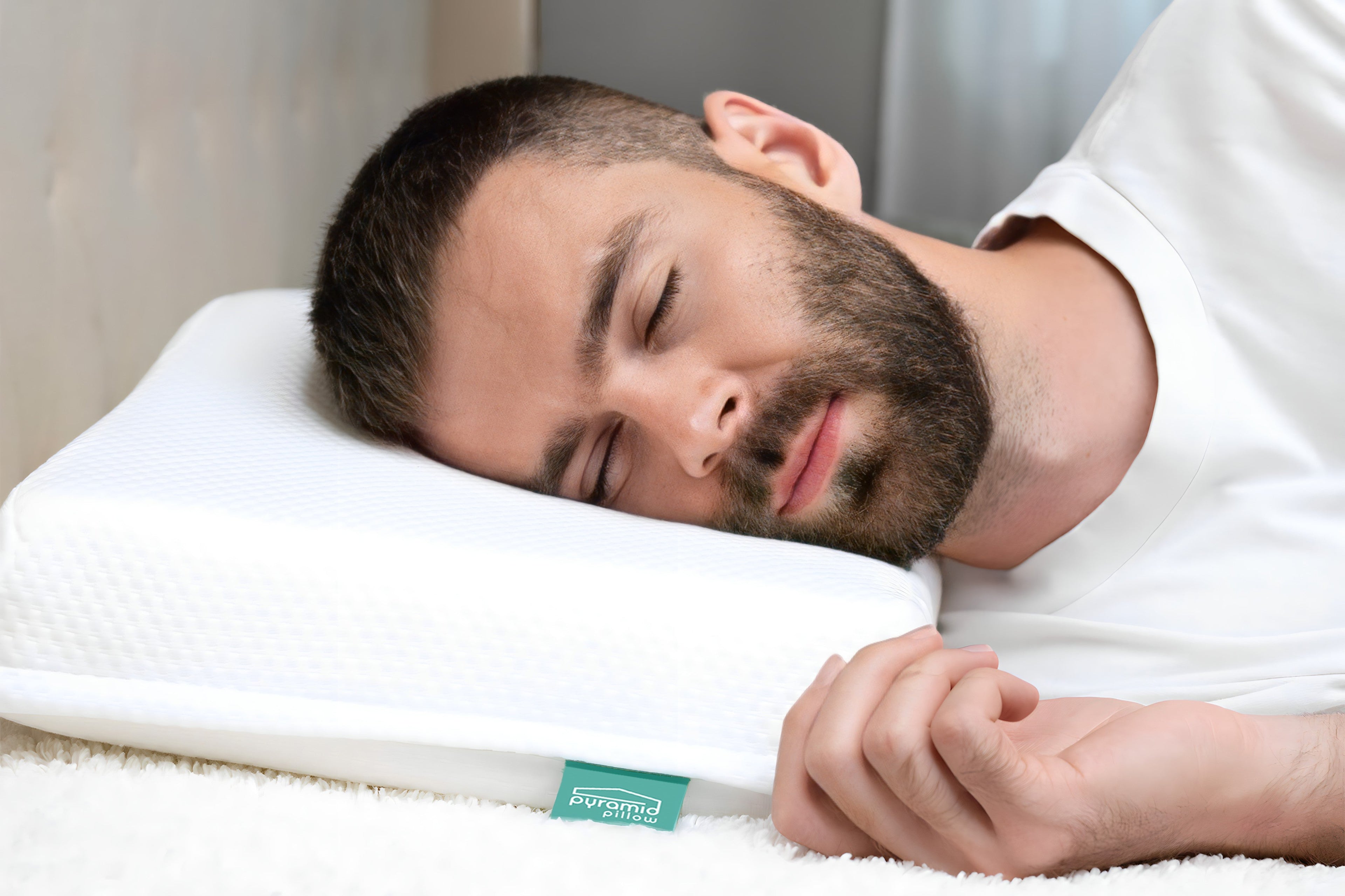 Man sleeping on a white anti-snoring Pyramid Pillow with a brand label in a bedroom setting